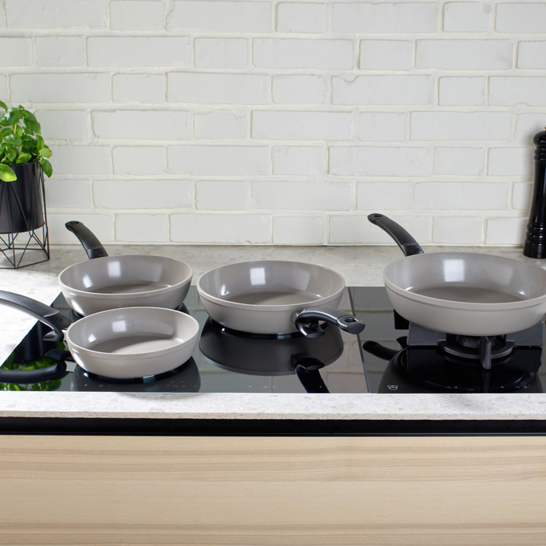 Set of ceramic Ceratal cookware on a stove with a white tiled wall background